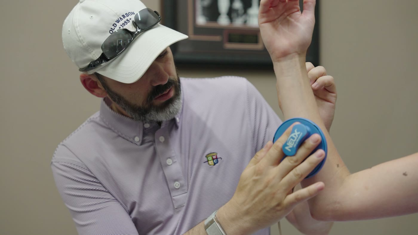A REM specialist applying NX Pro neuromuscular technology to a client's forearm during nervous-system mapping.